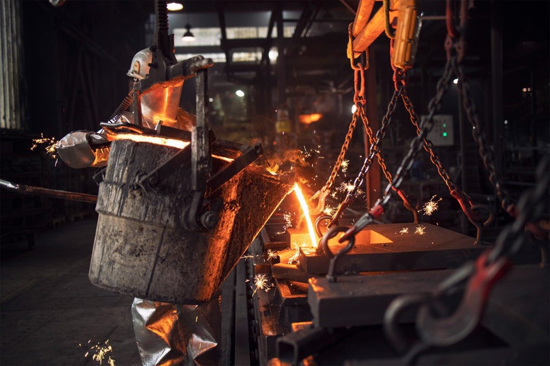 Arbeiter der Metallindustrie in Schutzanzug beim Gießen von Eisen