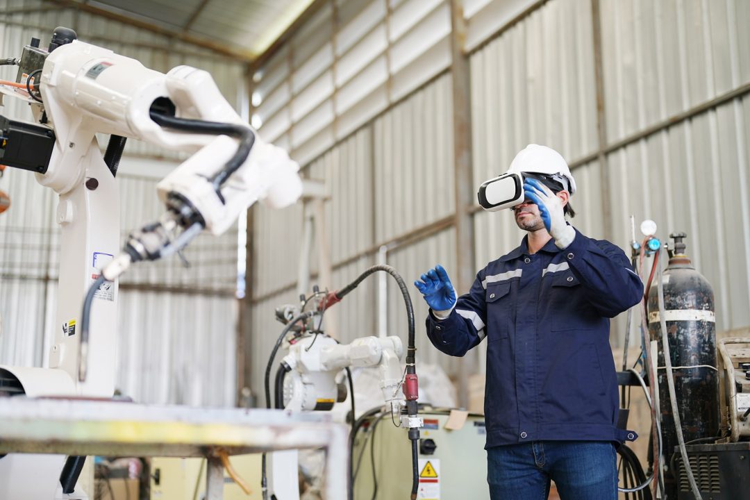 Wartung und Instandhaltung der Zukunft: ein Techniker mit VR Brille steht bei Roboterarm