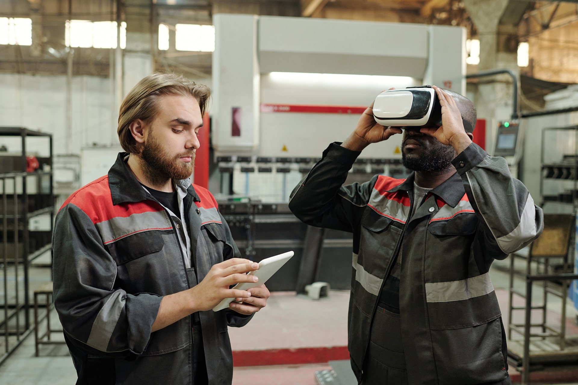 Instandhalter mit VR-Brille in Halle während anderer Techniker am AR-Tablet Daten kontrolliert