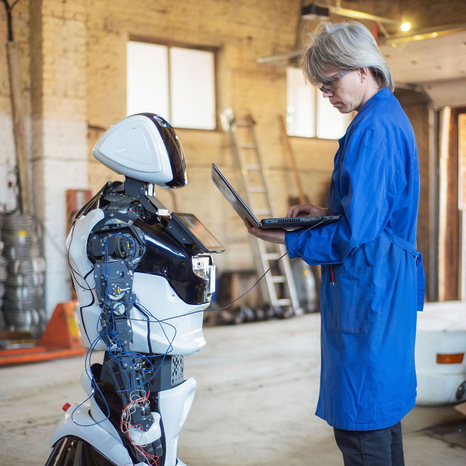 Techniker steht vor Roboter, der an Laptop angeschlossen ist.